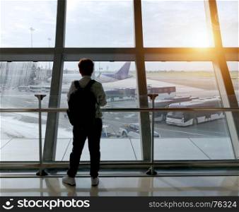 Travel concept. Young traveler with backpack at the airport looking through the window at planes waiting for flight.