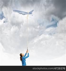Travel concept. Young woman holding flying airplane with rope