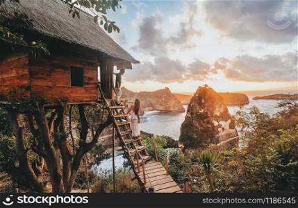 Travel Couple looking sunrise view Tree House with Daimond beach, Nusa Penida island Bali ,Indonesia