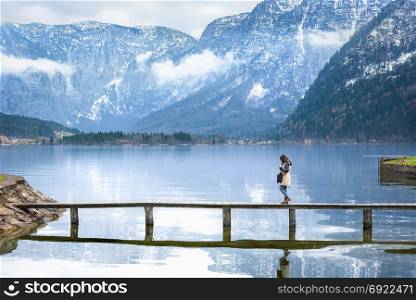 Travel destination theme image with a woman walking on a narrow deck that crosses the Hallstatter lake, surrounded by the Austrian Alps mountains.