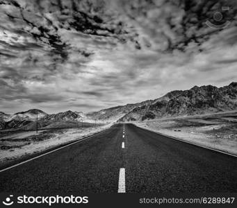 Travel forward concept background - road in Himalayas with mountains and dramatic clouds. Ladakh, Jammu and Kashmir, India. Black and white version