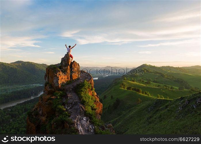 Travel, freedom leadership and real life concept - man standing on top of cliff in summer beauty sunset in Altai mountains. Man standing on top of cliff