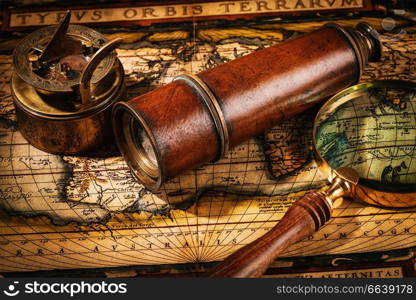 Travel geography navigation concept background - old vintage retro compass with sundial, spyglass and magnifying glass on ancient world map. Old vintage compass on ancient map