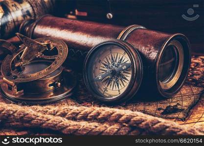 Travel geography navigation concept still life background - old vintage retro compass with sundial, spyglass and rope on ancient world map. Old vintage compass on ancient map