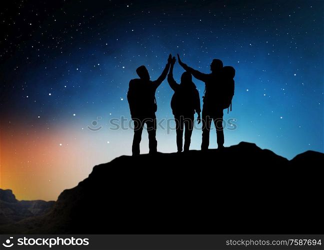 travel, hike and success concept - group of travelers or friends making high five gesture on edge of mountain over starry night sky or space background. travelers making high five over starry night sky
