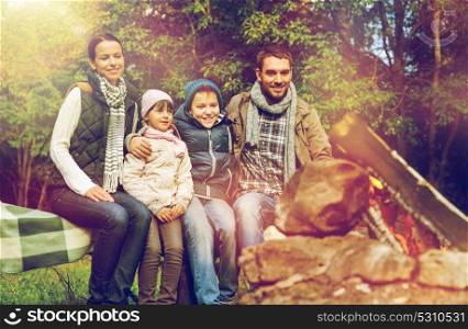 travel, hike and tourism concept - happy family sitting on bench and talking at camp near campfire in woods. happy family sitting on bench at camp fire