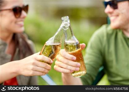 travel, hike, drinks, leisure and people concept - close up of happy couple clinking glass bottles and drinking cider or beer at campsite