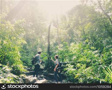 Travel hiking and ecotourism concept from asian couple traveler with backpack exploring the beautiful tropical rainforest and enjoying see nature view with sunlight through trees.