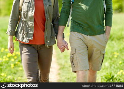 travel, hiking, backpacking, tourism and people concept - close up of couple with backpacks holding hands and walking along country road