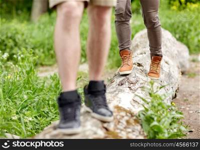 travel, hiking, backpacking, tourism and people concept - close up of couple legs walking along fallen tree trunk outdoors
