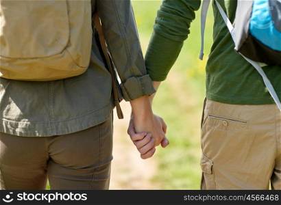 travel, hiking, backpacking, tourism and people concept - close up of couple with backpacks holding hands and walking along country road