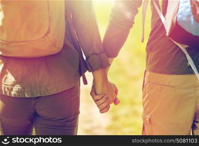 travel, hiking, backpacking, tourism and people concept - close up of couple with backpacks holding hands and walking along country road. close up of couple with backpacks holding hands