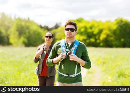 travel, hiking, backpacking, tourism and people concept - couple with backpacks walking along country road outdoors