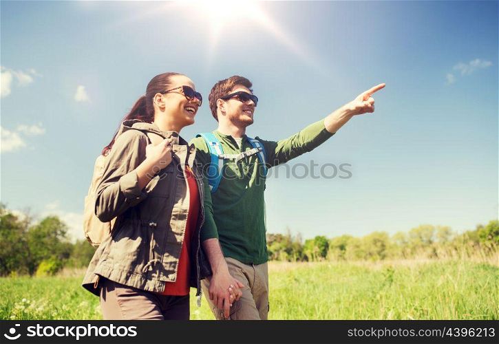 travel, hiking, backpacking, tourism and people concept - happy couple with backpacks walking along country road outdoors and pointing finger to something. happy couple with backpacks hiking outdoors. happy couple with backpacks hiking outdoors