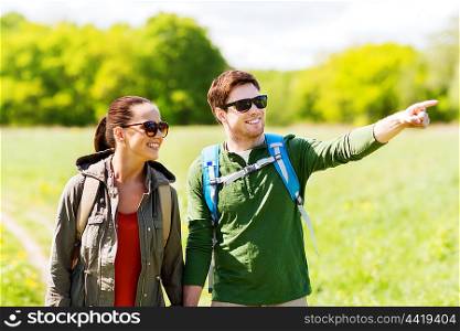 travel, hiking, backpacking, tourism and people concept - happy couple with backpacks walking along country road outdoors and pointing finger to something