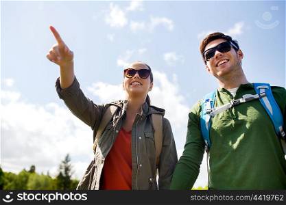 travel, hiking, backpacking, tourism and people concept - happy couple with backpacks walking outdoors and pointing finger to something