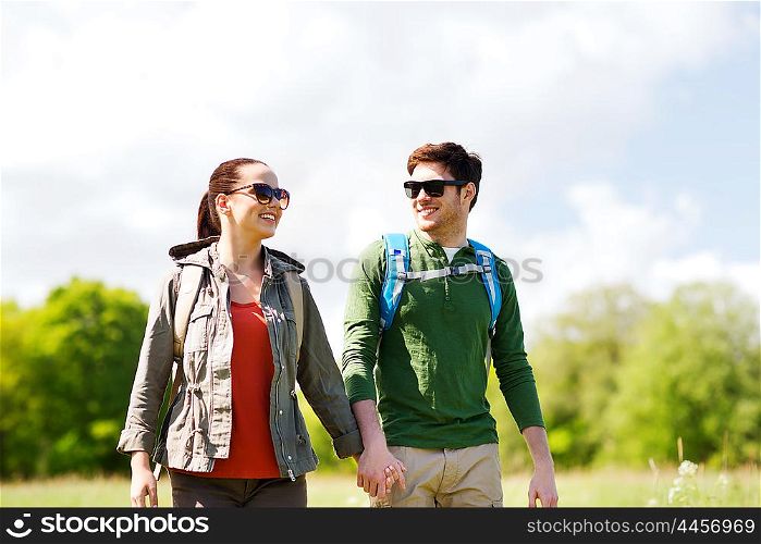 travel, hiking, backpacking, tourism and people concept - happy couple with backpacks holding hands and walking outdoors