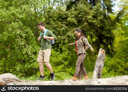 travel, hiking, backpacking, tourism and people concept - happy couple with backpacks walking along fallen tree trunk outdoors