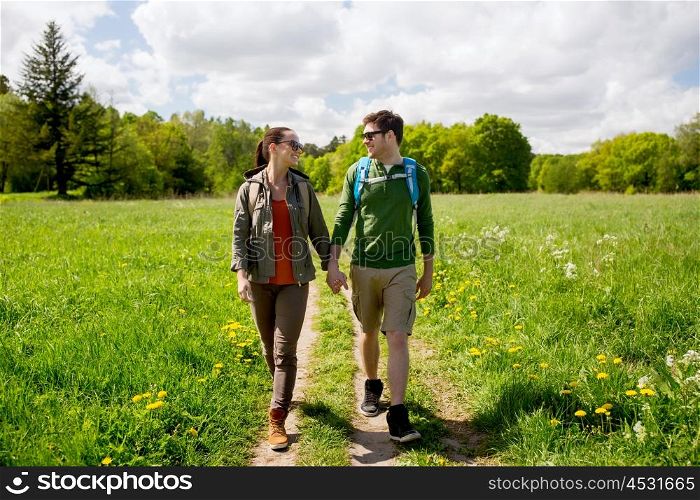 travel, hiking, backpacking, tourism and people concept - happy couple with backpacks holding hands and walking along country road outdoors