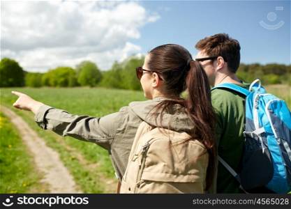 travel, hiking, backpacking, tourism and people concept - happy couple with backpacks walking along country road and pointing finger to something