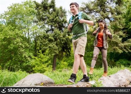 travel, hiking, backpacking, tourism and people concept - happy couple with backpacks walking along fallen tree trunk outdoors
