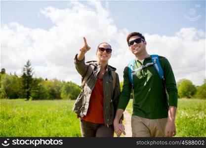 travel, hiking, backpacking, tourism and people concept - happy couple with backpacks walking along country road outdoors and pointing finger to something
