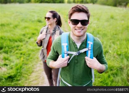 travel, hiking, backpacking, tourism and people concept - happy couple with backpacks walking along country road outdoors