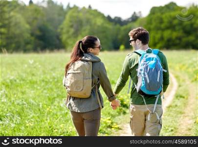 travel, hiking, backpacking, tourism and people concept - happy couple with backpacks holding hands and walking along country road