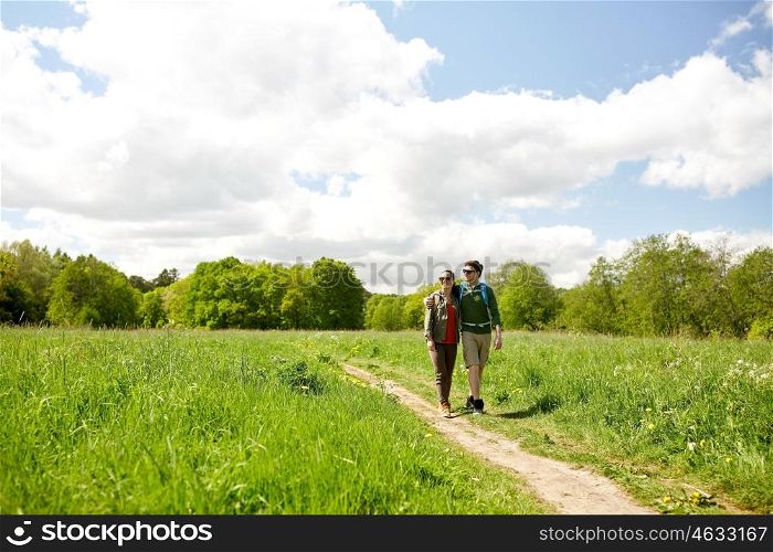 travel, hiking, backpacking, tourism and people concept - happy couple with backpacks hugging and walking along country road