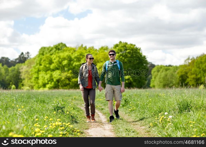 travel, hiking, backpacking, tourism and people concept - happy couple with backpacks holding hands and walking along country road