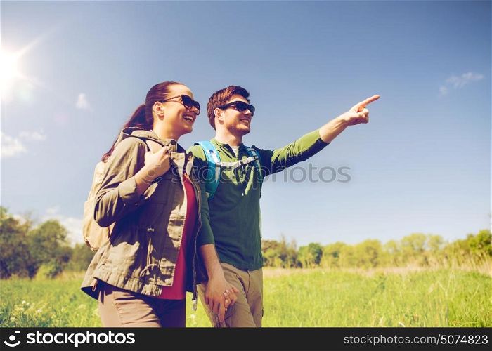 travel, hiking, backpacking, tourism and people concept - happy couple with backpacks walking along country road outdoors and pointing finger to something. happy couple with backpacks hiking outdoors