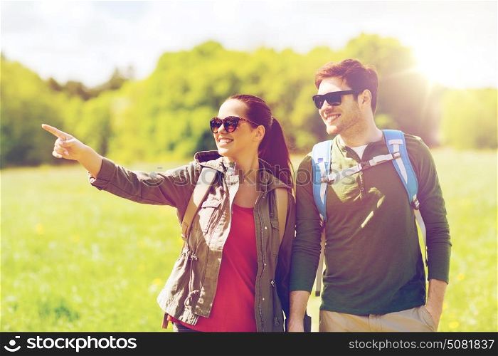 travel, hiking, backpacking, tourism and people concept - happy couple with backpacks walking outdoors and pointing finger to something. happy couple with backpacks hiking outdoors