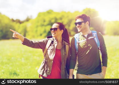 travel, hiking, backpacking, tourism and people concept - happy couple with backpacks walking outdoors and pointing finger to something. happy couple with backpacks hiking outdoors