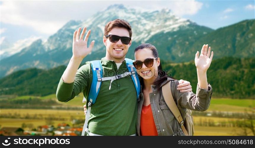 travel, hiking, backpacking, tourism and people concept - happy couple with backpacks waving hands over alps mountains background. happy couple with backpacks traveling in highlands. happy couple with backpacks traveling in highlands