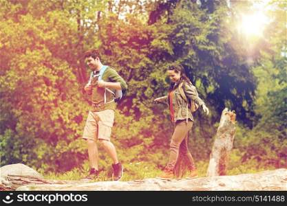 travel, hiking, backpacking, tourism and people concept - happy couple with backpacks walking along fallen tree trunk outdoors. happy couple with backpacks hiking outdoors