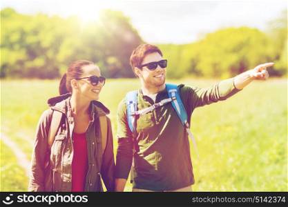 travel, hiking, backpacking, tourism and people concept - happy couple with backpacks walking along country road outdoors and pointing finger to something. happy couple with backpacks hiking outdoors