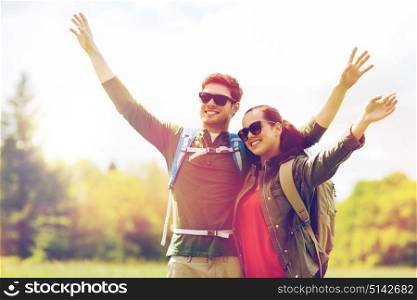 travel, hiking, backpacking, tourism and people concept - happy couple with backpacks waving hands and walking along country road outdoors. happy couple with backpacks hiking outdoors