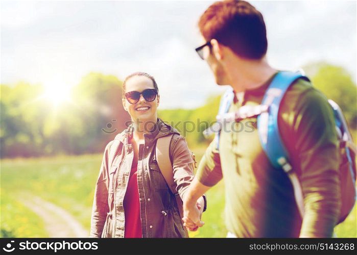 travel, hiking, backpacking, tourism and people concept - happy couple with backpacks holding hands and walking along country road outdoors. happy couple with backpacks hiking outdoors