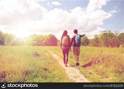travel, hiking, backpacking, tourism and people concept - happy couple with backpacks holding hands and walking along country road. happy couple with backpacks hiking outdoors