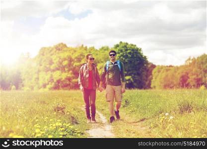 travel, hiking, backpacking, tourism and people concept - happy couple with backpacks holding hands and walking along country road. happy couple with backpacks hiking outdoors