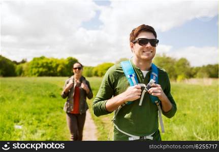 travel, hiking, backpacking, tourism and people concept - happy couple with backpacks walking along country road outdoors