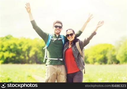 travel, hiking, backpacking, tourism and people concept - happy couple with backpacks waving hands and walking along country road outdoors. happy couple with backpacks hiking outdoors. happy couple with backpacks hiking outdoors