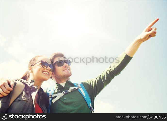 travel, hiking, backpacking, tourism and people concept - happy couple with backpacks outdoors pointing finger to something in sky. happy couple with backpacks hiking outdoors. happy couple with backpacks hiking outdoors