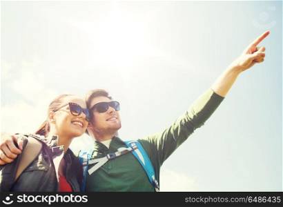 travel, hiking, backpacking, tourism and people concept - happy couple with backpacks outdoors pointing finger to something in sky. happy couple with backpacks hiking outdoors. happy couple with backpacks hiking outdoors
