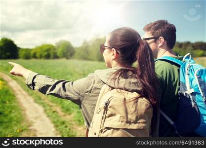 travel, hiking, backpacking, tourism and people concept - happy couple with backpacks walking along country road and pointing finger to something. happy couple with backpacks hiking outdoors. happy couple with backpacks hiking outdoors
