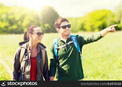 travel, hiking, backpacking, tourism and people concept - happy couple with backpacks walking along country road outdoors and pointing finger to something. happy couple with backpacks hiking outdoors. happy couple with backpacks hiking outdoors