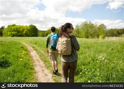 travel, hiking, backpacking, tourism and people concept - happy couple with backpacks walking along country road