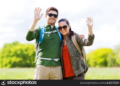 travel, hiking, backpacking, tourism and people concept - happy couple with backpacks waving hands outdoors