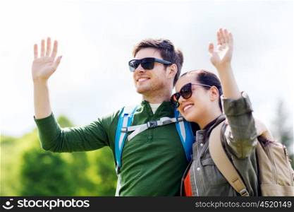 travel, hiking, backpacking, tourism and people concept - happy couple with backpacks waving hands outdoors