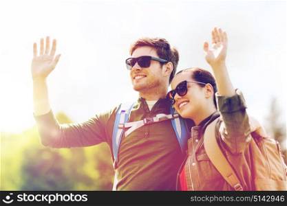 travel, hiking, backpacking, tourism and people concept - happy couple with backpacks waving hands outdoors. happy couple with backpacks hiking outdoors